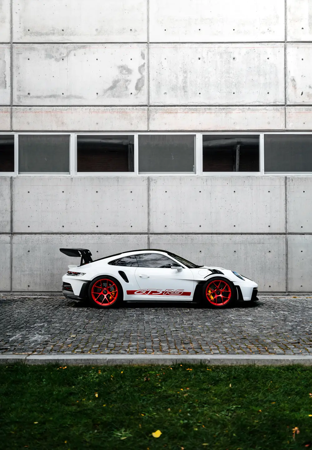 Porsche 911 GT3 RS branco de perfil, diante de um muro de concreto